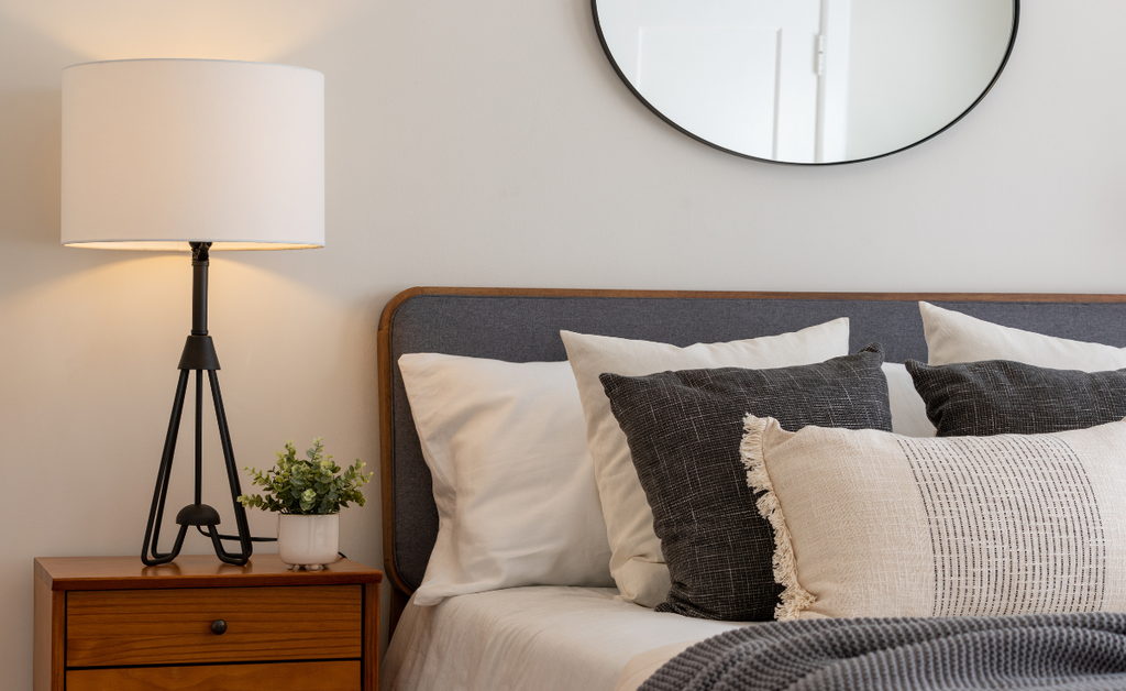 White and gray bedroom with an oval mirror over the bed.