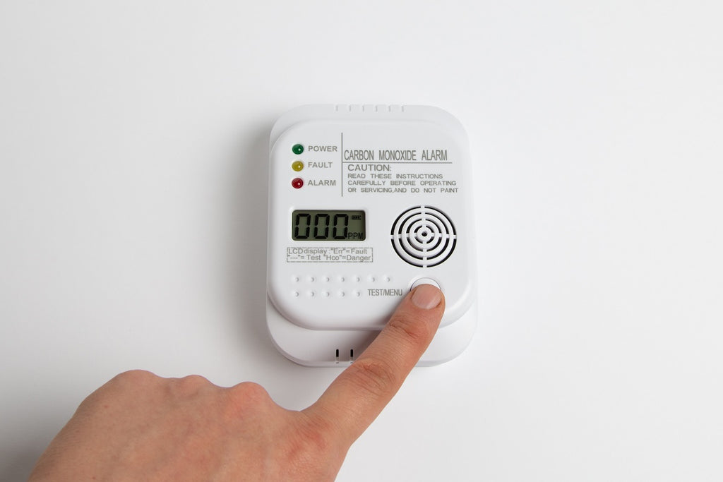 Carbon monoxide detector on a white wall with person pressing a button.