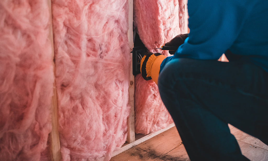 Person installing insulation in an exposed wall.