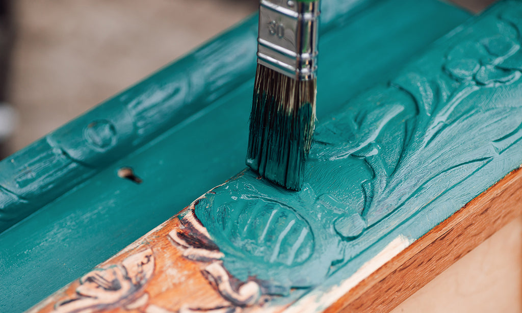 Close up of paint brush applying teal paint to trim.