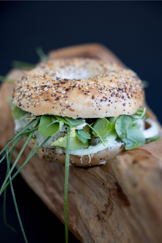 Everything bagel loaded with greens and cream cheese displayed on a log