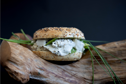 Everything bagel loaded with greens and cream cheese, displayed on a log from a different angle