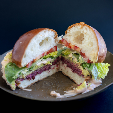 Large bean burger with dripping sauce cheese slice tomato lettuce and bun, cut in half