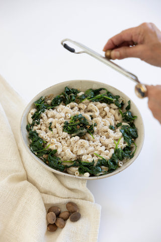 Creamy mac and cheese with greens in bowl, hands adding garnish