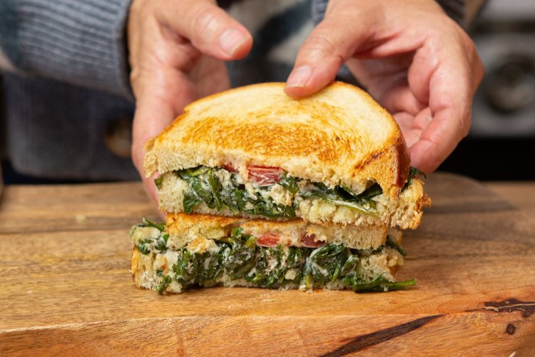 Hands holding spinach garlic grilled cheese sandwich cut in half