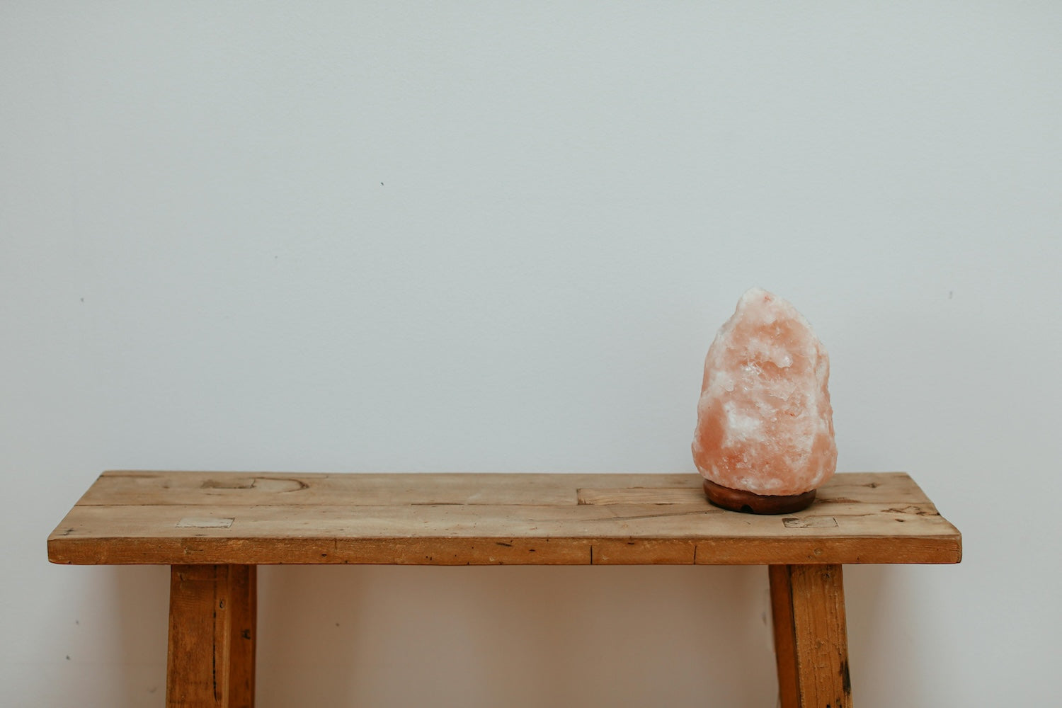 Himalayan salt lamp on a rustic wooden bench against a white wall.