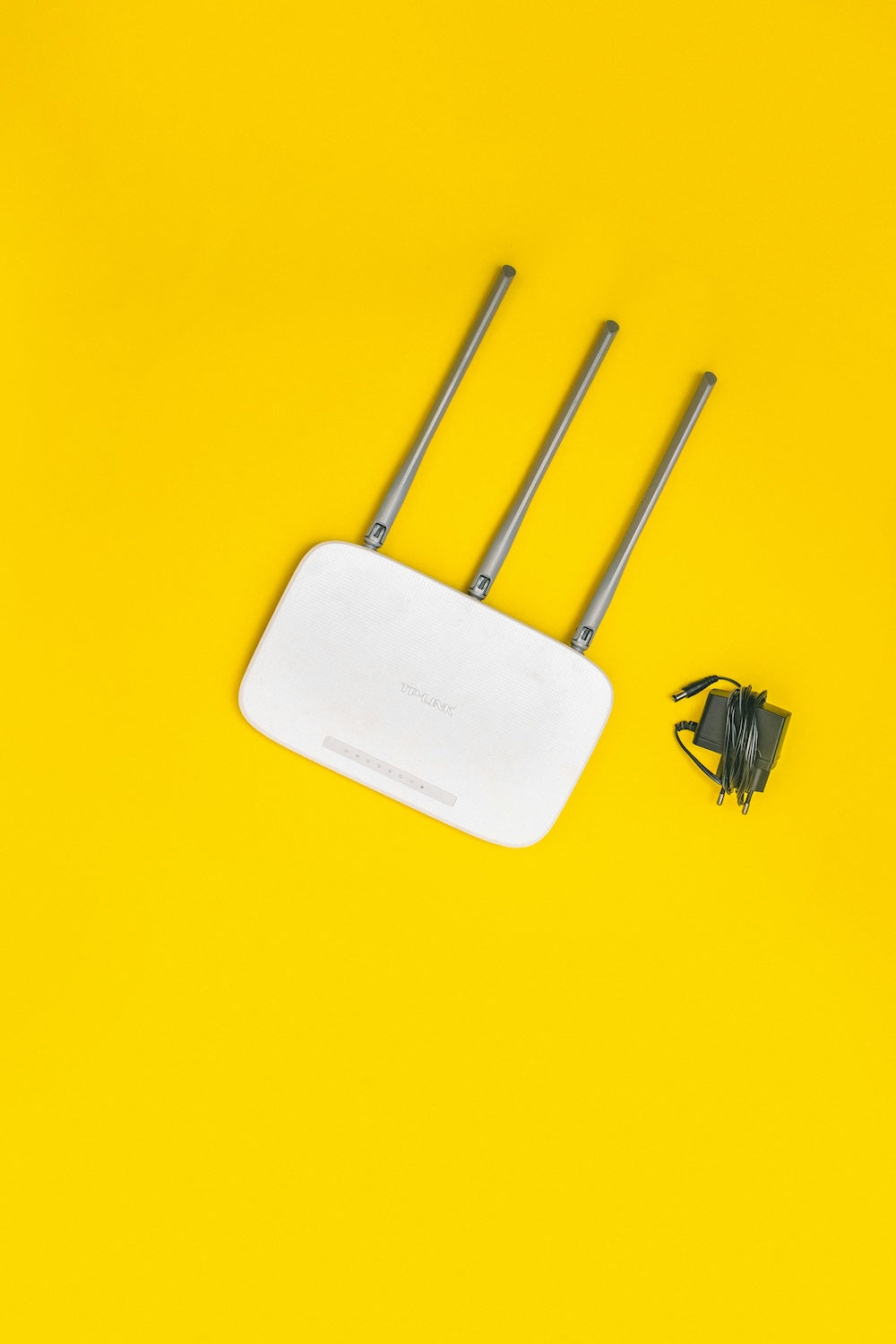 White Wi-Fi router with three antennas and a black cable on a yellow background.