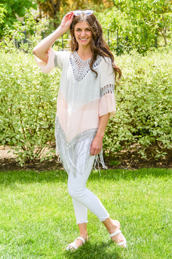 Woman wearing a poncho and white jeans outside on a sunny day