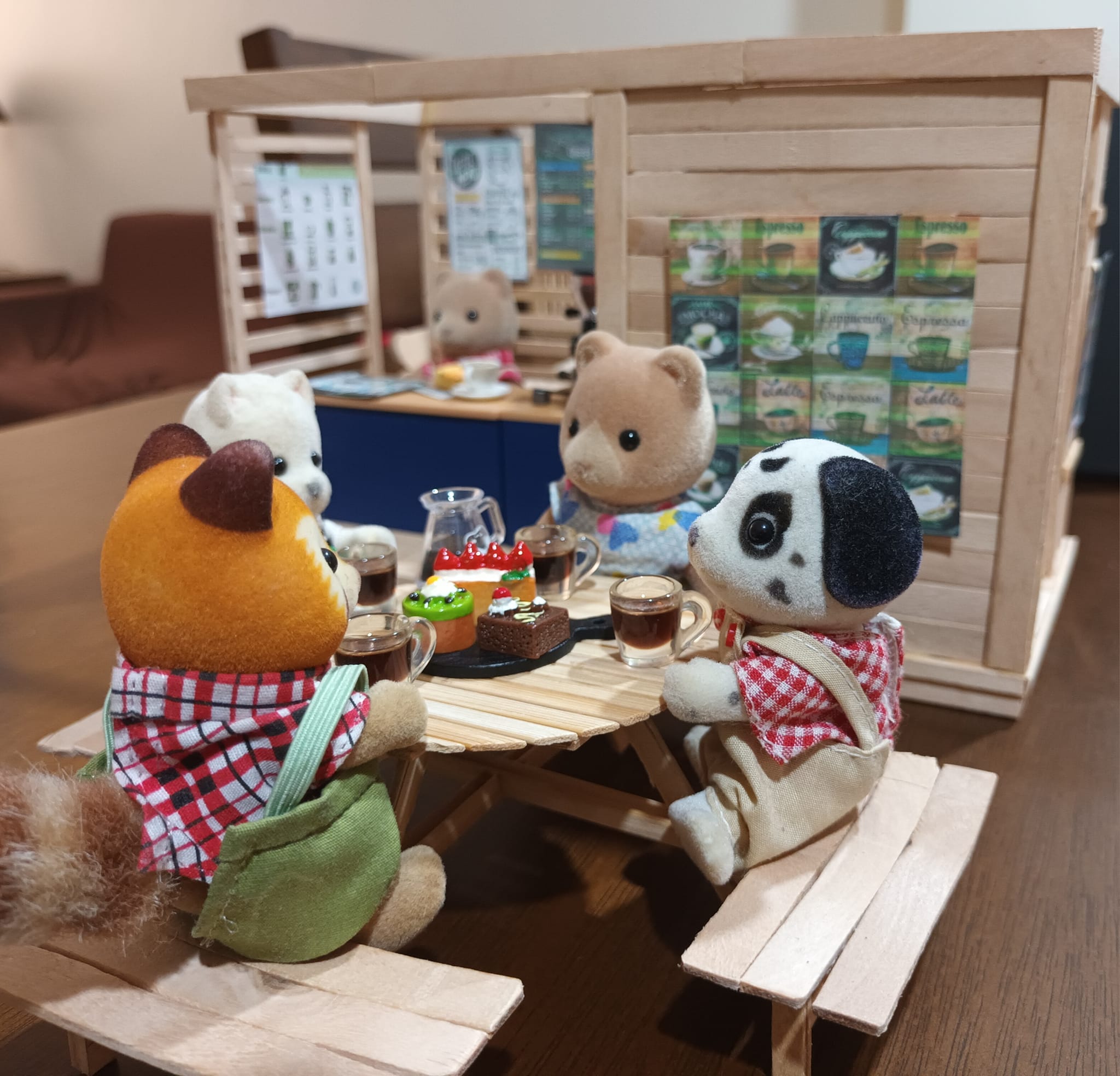 4 Calico Critters sitting at a picnic table, drinking coffee and eating cakes.