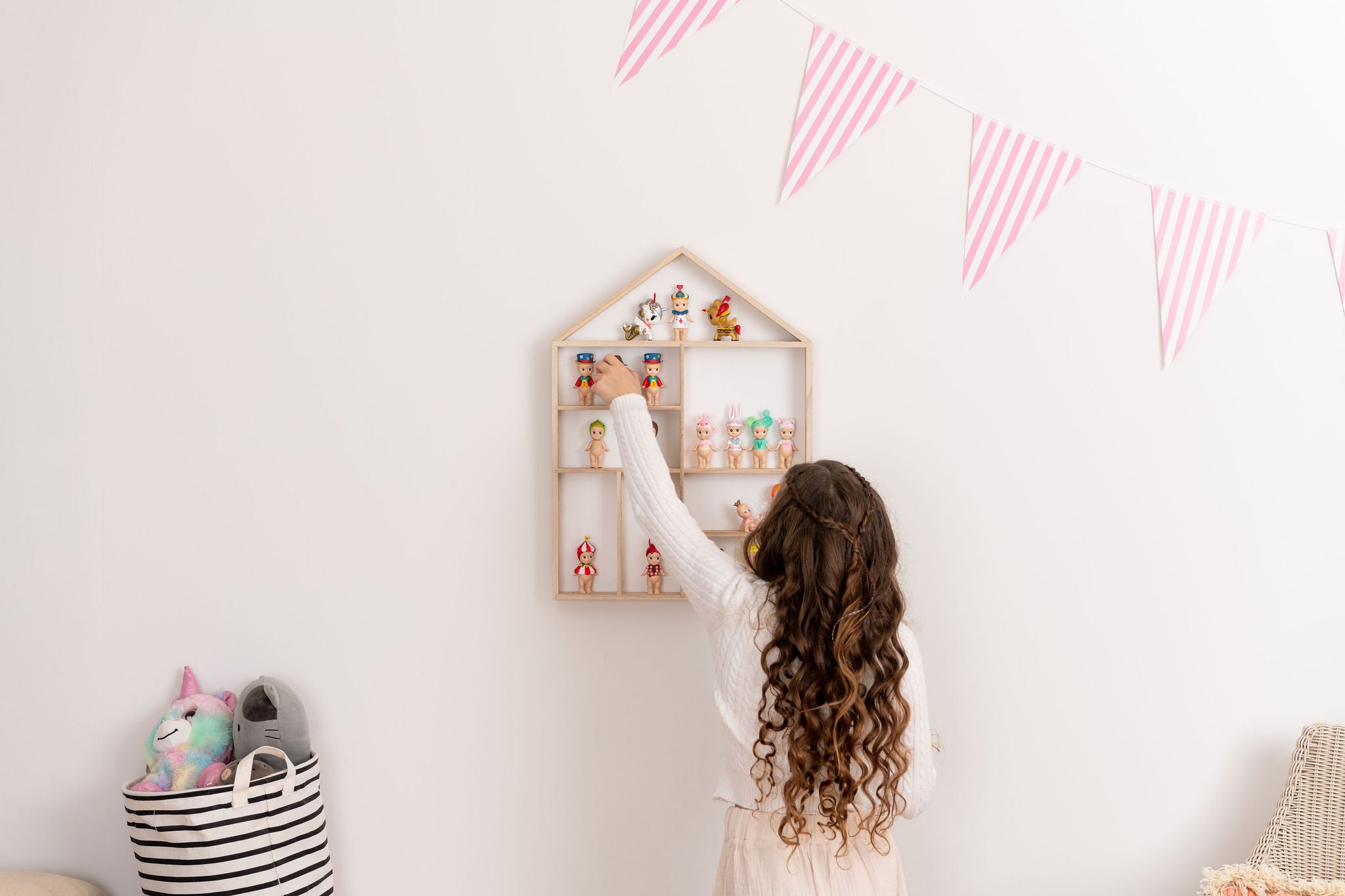 Girl facing the wall playing with Sonny Angels on a house-shaped wooden toy display shelf that is hung on the wall