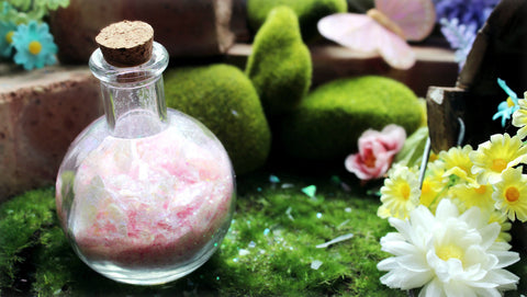 Pink fairy dust in a potion bottle stands in an artificial fairy garden