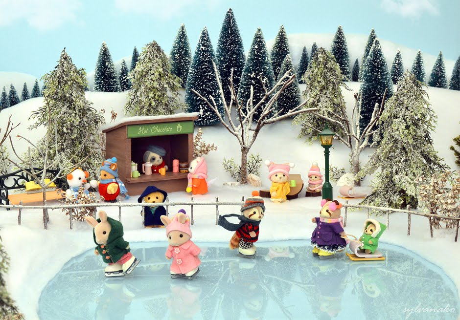 Calico Critters ice skating on a frozen pond, along side a hot chocolate stall, snowed trees, and wooden fences.