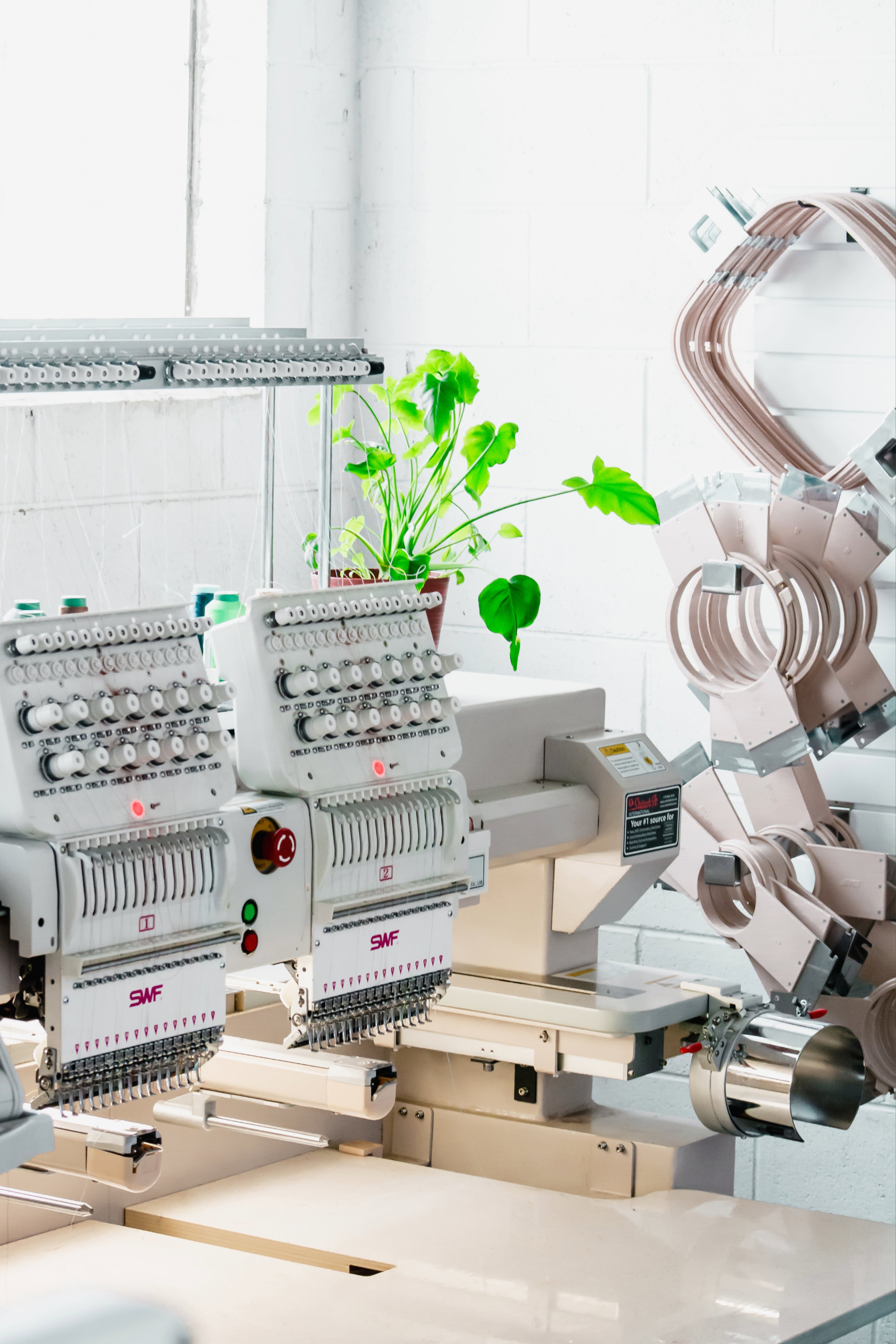 Commercial embroidery machine with plant on top and embroidery hoops in screen printing and embroidery shop in Brookfield, Wisconsin.