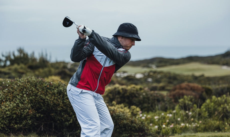 a man swings his golf club while wearing a men's golf rain jacket