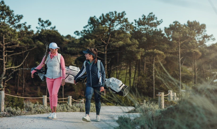 Two women walk through a golf course wearing women's wind jackets