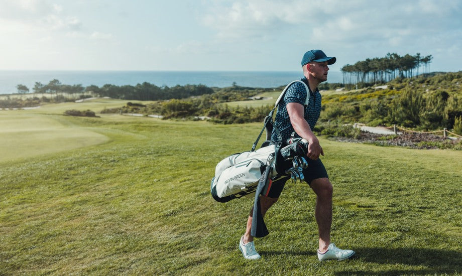 a man walks across a golf course carrying his golf bag.