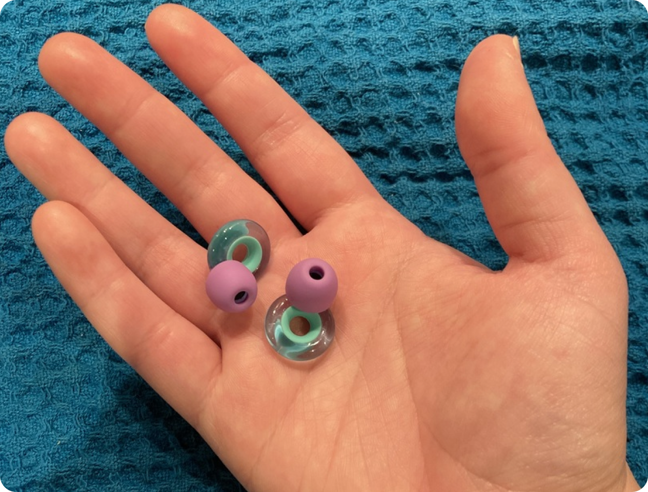 Hand holding a pair of purple earplugs on a blue textured cloth.