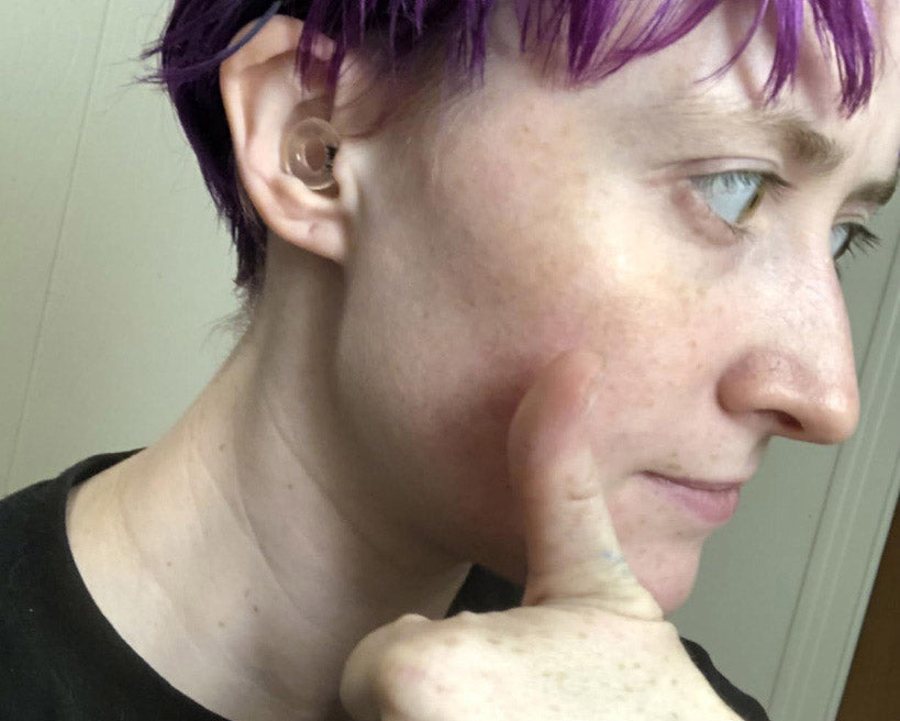 Profile of a person with purple hair pressing on their cheek with a thoughtful expression.