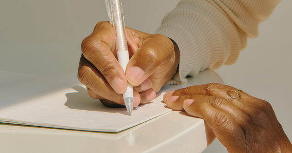 Black Woman holding a pen and beginning to write on paper.