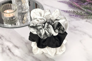 Celestial Silk large white marble, ivory and black silk scrunchies stacked on marble counter with lavender plant and a candle in the background