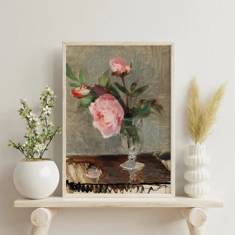 Painting by Berthe Morisot titled 'Peonies' showing delicate pink peonies in a glass vase on a table. The art print is framed in a white frame and sits on a shelf.