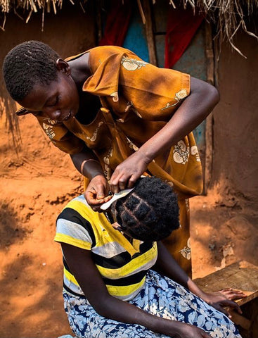 Image of a traditional black woman making a girl’s hair. 