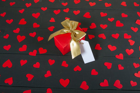 Red paper hearts on black backdrop with a red gift box in the centre