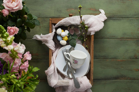 Wood tray of easter eggs and dishware next to pink flowers