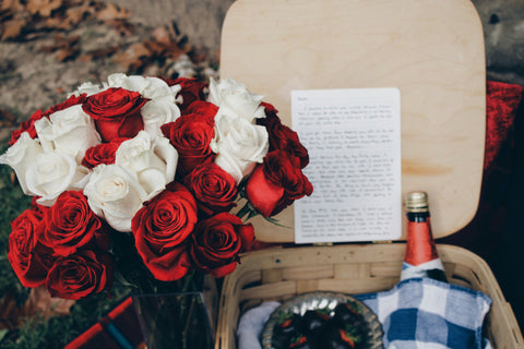 Red and white rose bouquet with letter and bottle in a basket