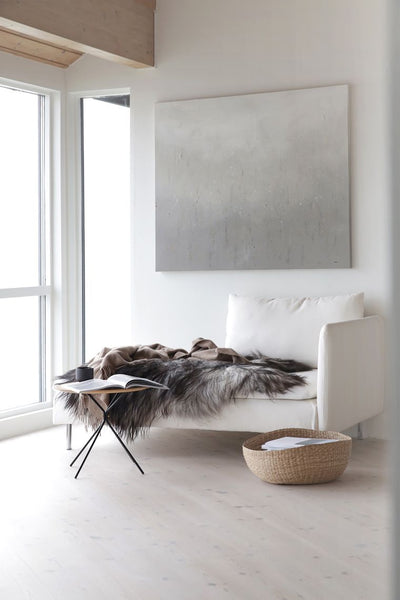 A minimal space with grey artwork and a day sofa with fur throw. A coffee table is placed in the most minimalist way with a little basket at the base.