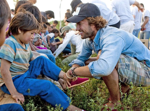 White man puts shoes on an indigenous child