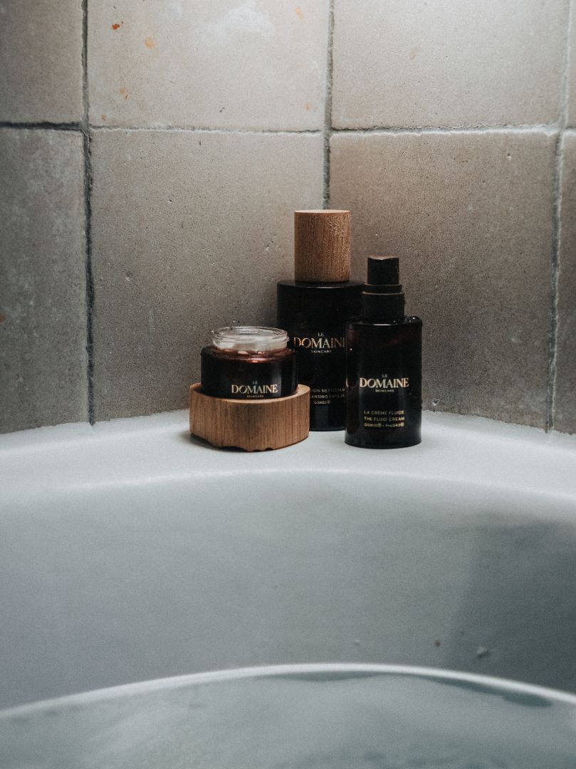 Cosmetic bottles on a bathroom ledge with neutral tiled background.