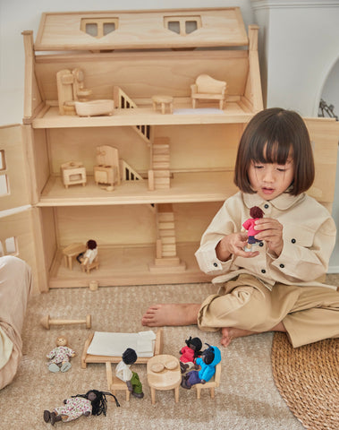 Child playing with dollhouse, dolls, and furniture