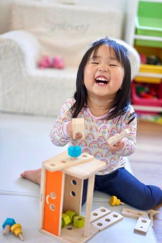 Child playing with PlanToys Robot Toolbox and laughing