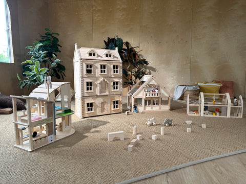 A group of wooden dollhouses and blocks on the floor of a playroom