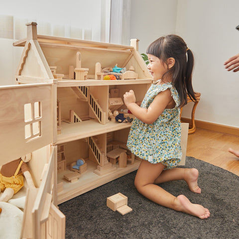 A young child sitting up and playing with a wooden dollhouse