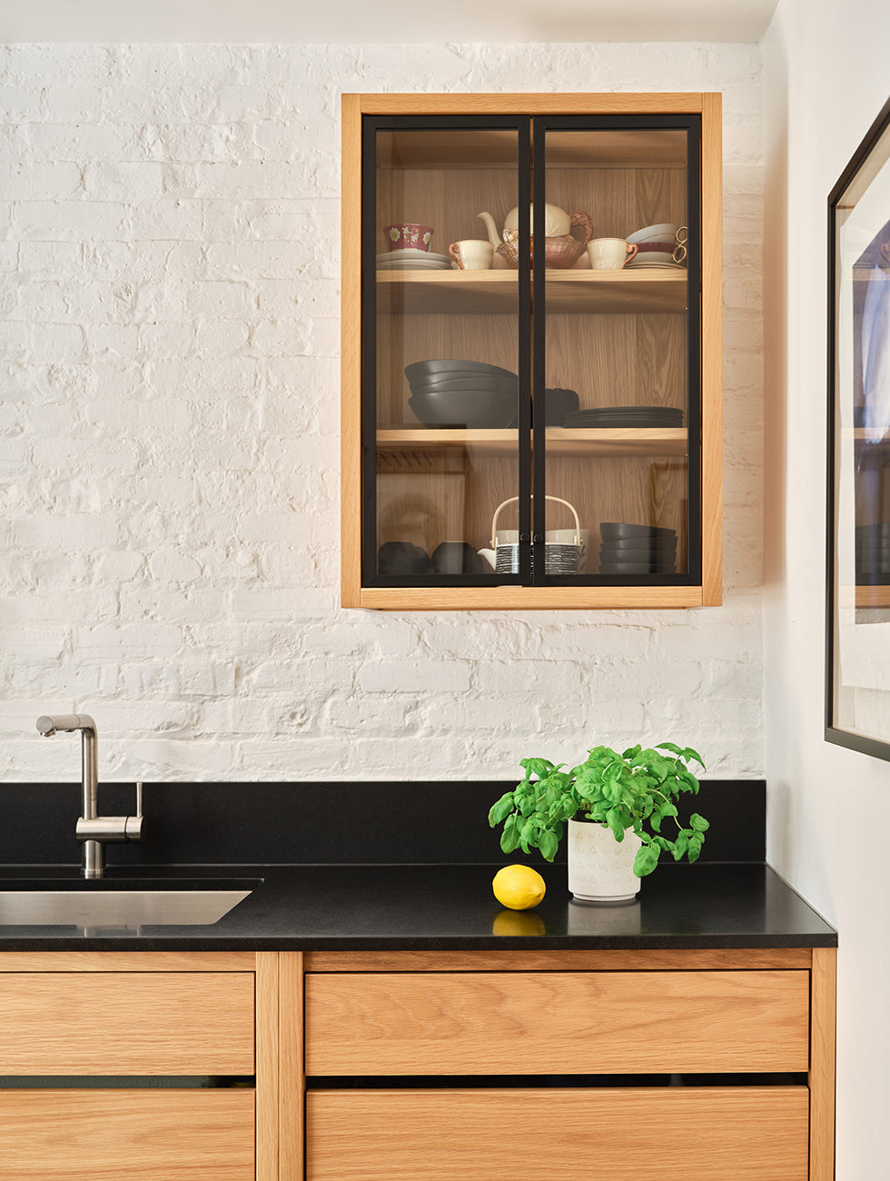 Cuisine minimaliste en chêne blanc avec comptoir noir et mini dosseret en quartz. Mur de brique blanche.