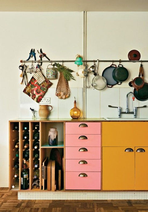 Colourful kitchen cabinets in pink and yellow, with metal utility rail for storage. 