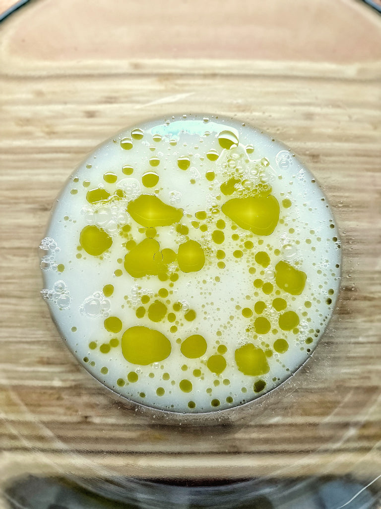 Overhead shot of a bowl of white liquid, bright green olive oil drops floating atop