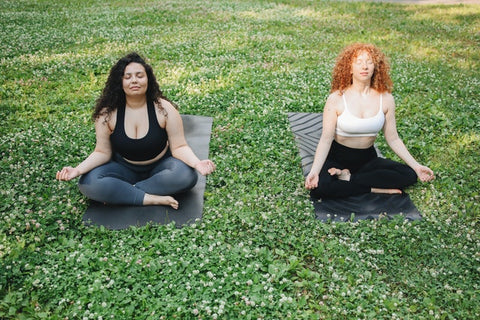 two-women-sitting-on-yoga-mats-on-the-grass