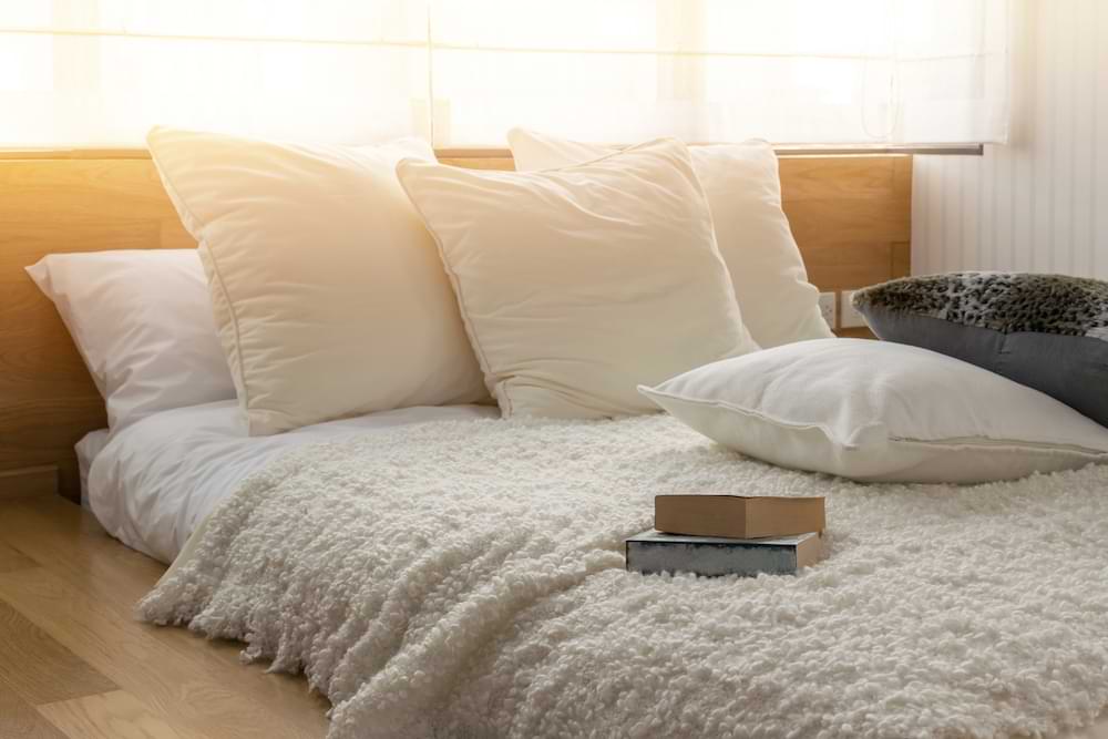 Cozy bedding in a sun-drenched room with books lying on the coverlet.