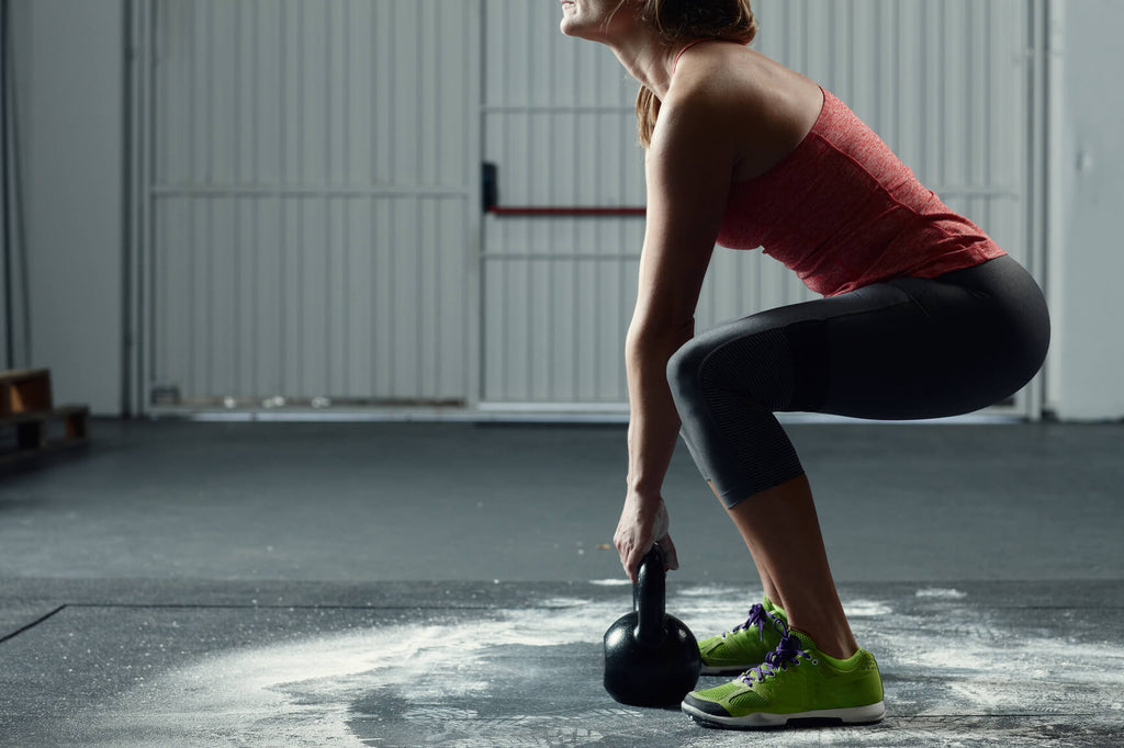 Athletic white woman in workout clothes doing squats with a kettle bell