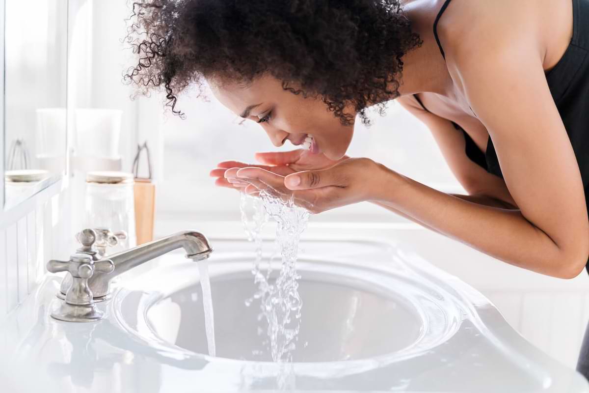 Black woman bending over a sink splashing water on her face