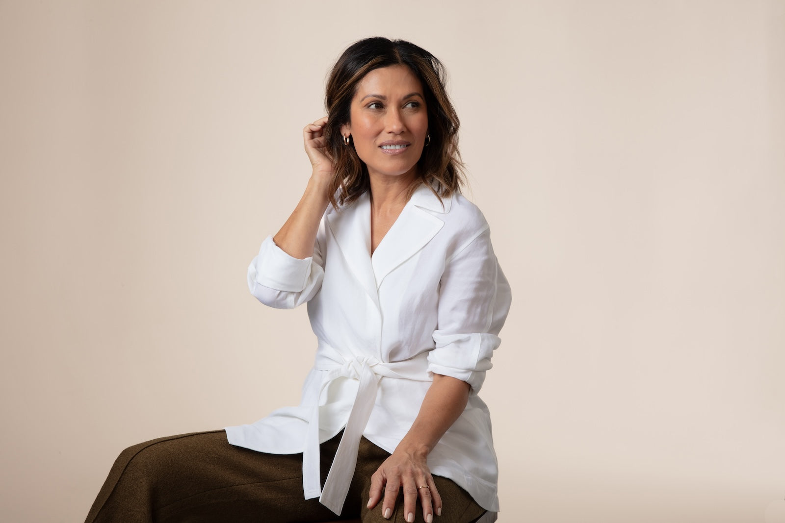 A beautiful Latina woman wearing a white blouse and gold hoop earrings, running her fingers through her hair