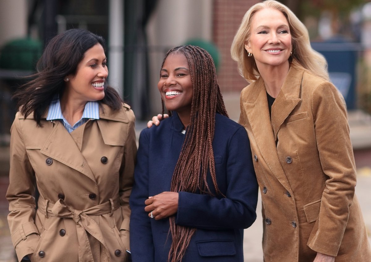 Three beautiful women smile together on a city street corner looking vibrant and happy