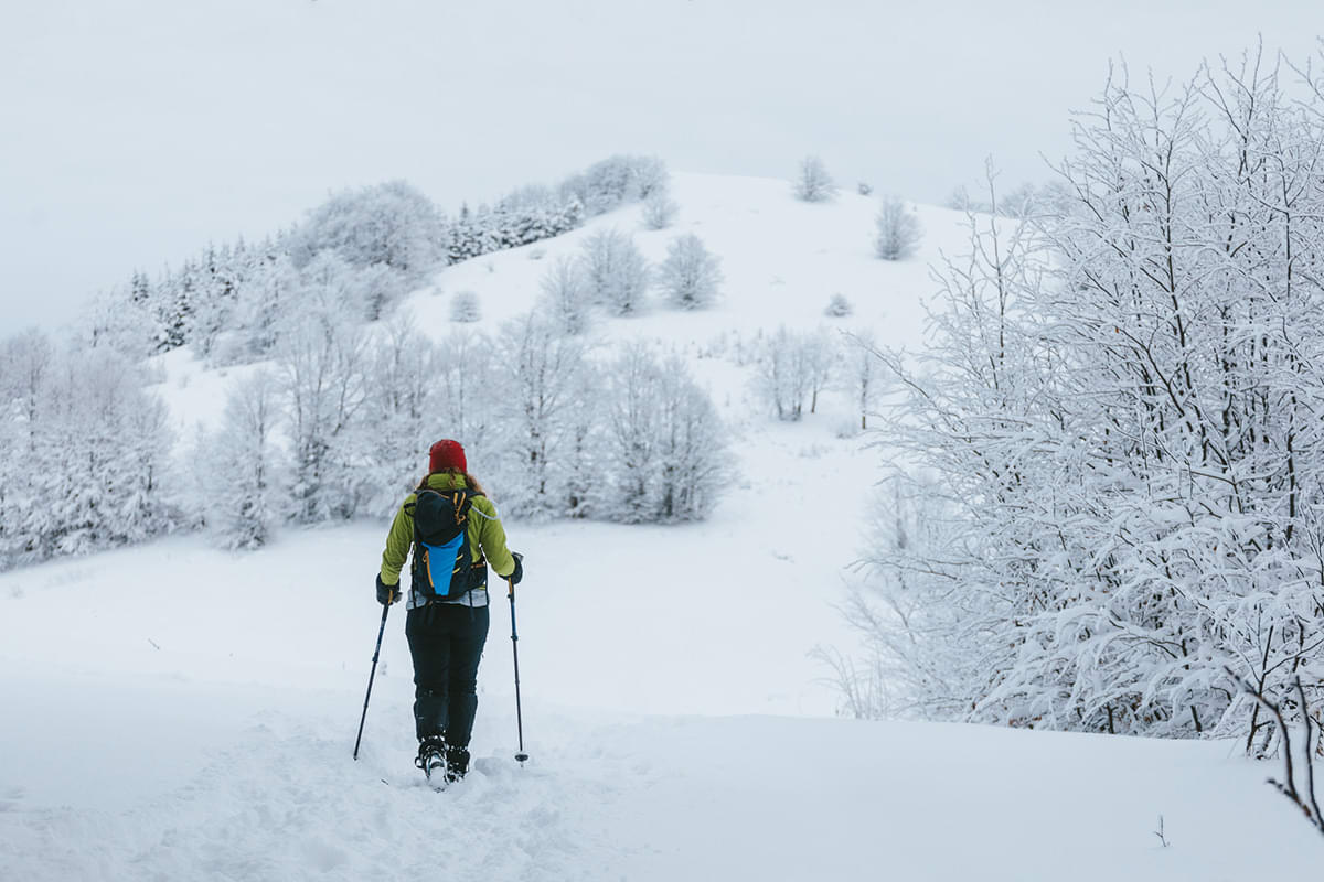 A woman in cold-weather gear hiking a beautiful snowy hill