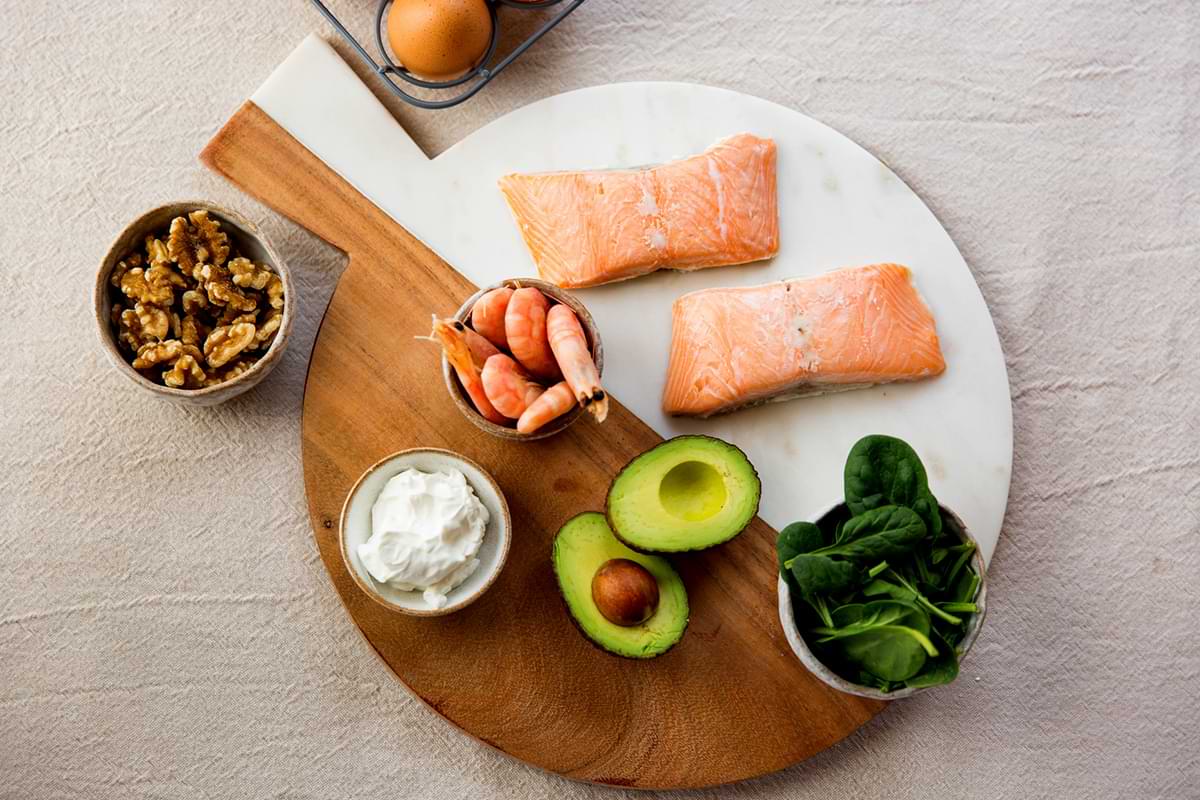 A charcuterie board covered with salmon, shrimp, avocado, spinach, walnuts, and hummus