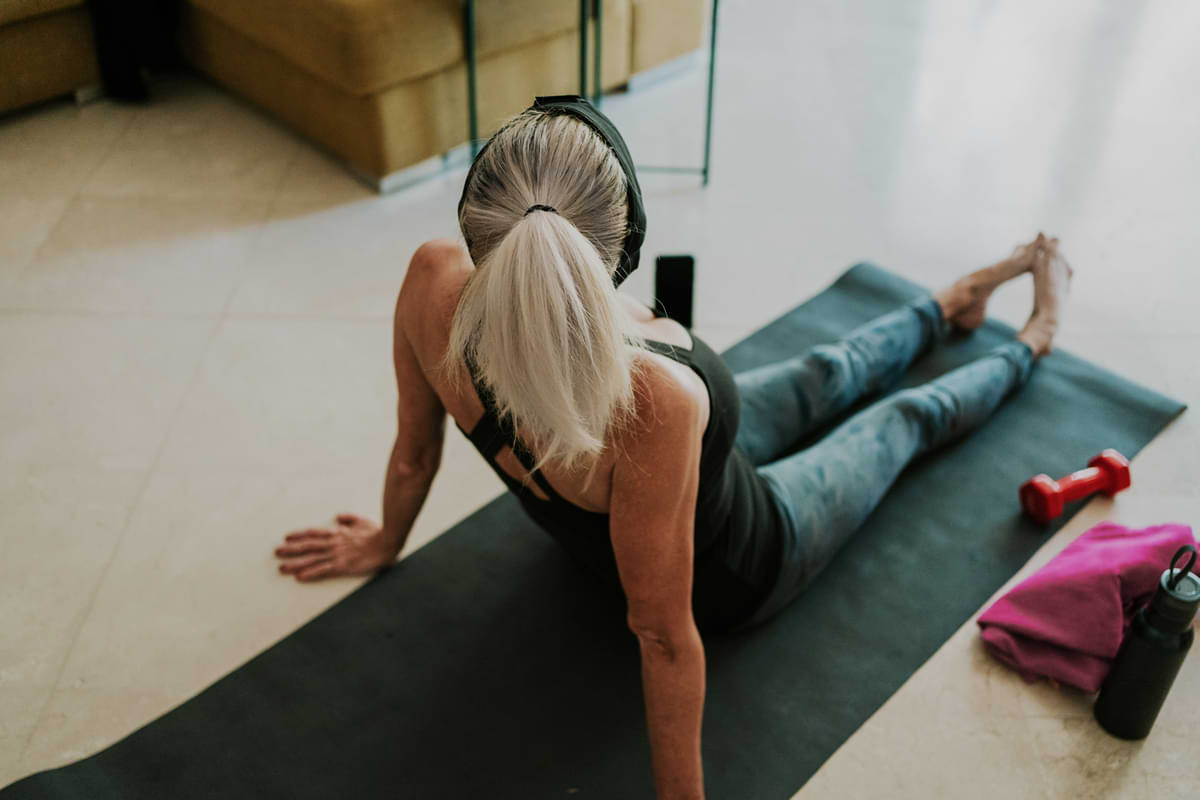 White woman in yoga clothes sitting on a yoga mat stretching.