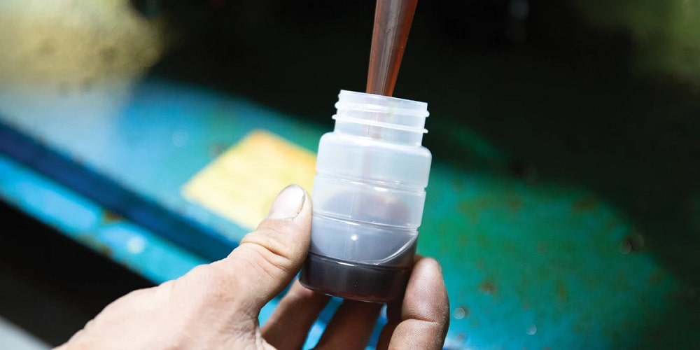 Closeup of a compressor oil sampling bottle showing someone filling the bottle with dark oil from a sampling tube