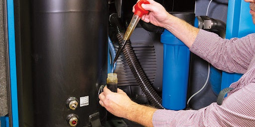 a man sampling oil from the air compressor sump using a baster to add oil to a small container